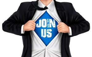 Man tearing open his suit jacket and shirt, revealing a blue t-shirt with white letters saying, "Join Us"